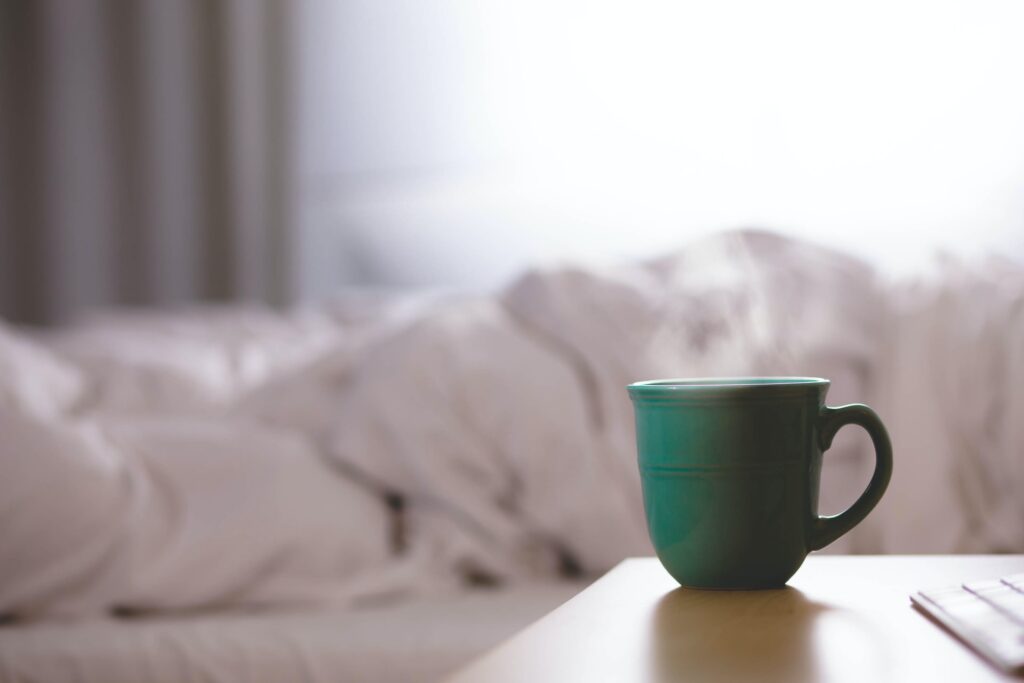 green mug steaming on a bedside table